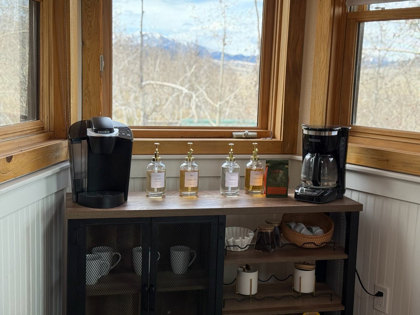 Coffee bar with brewers and flavored syrups in front of a snowy mountain view